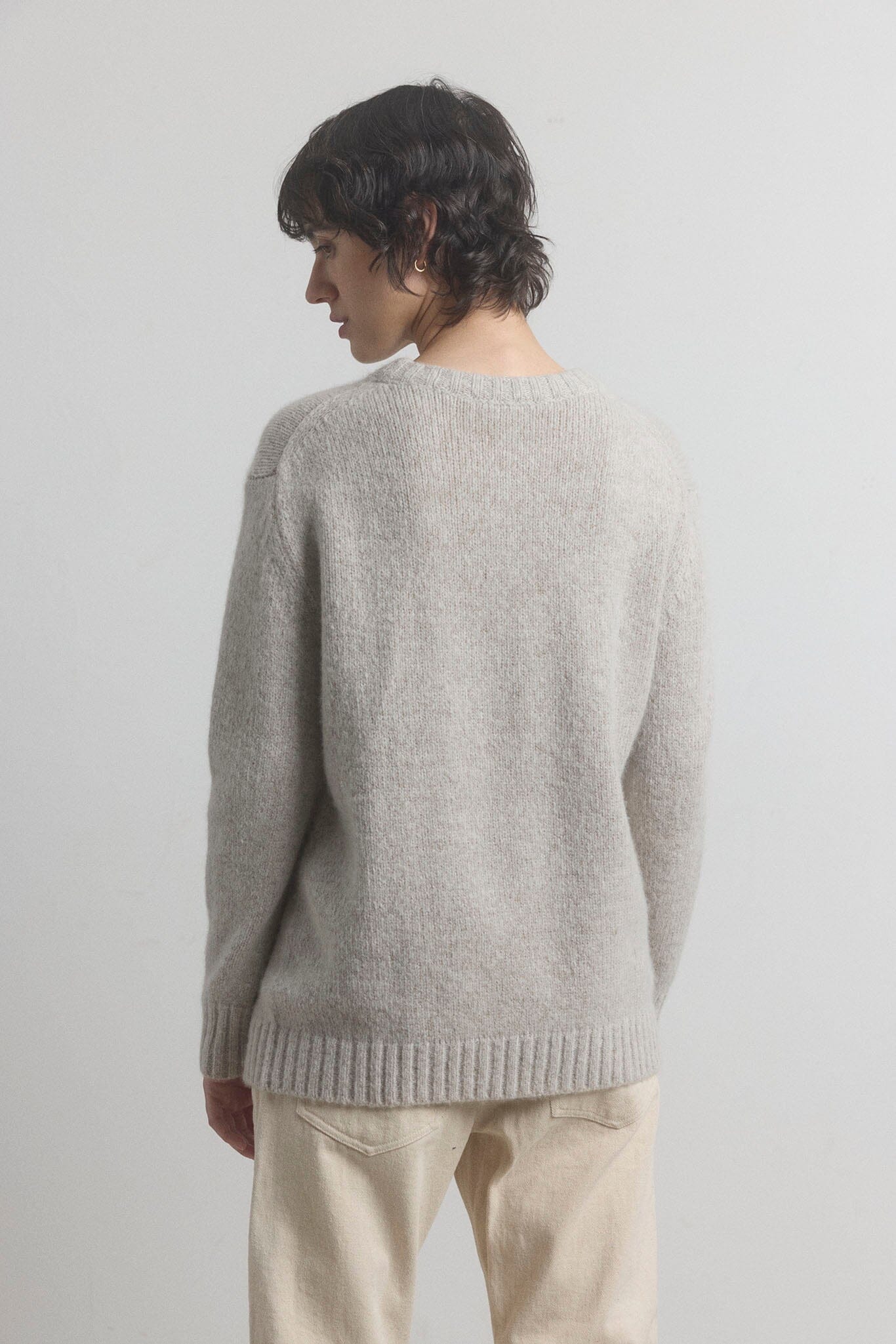Woman wearing a gray sweater and beige pants against a plain background