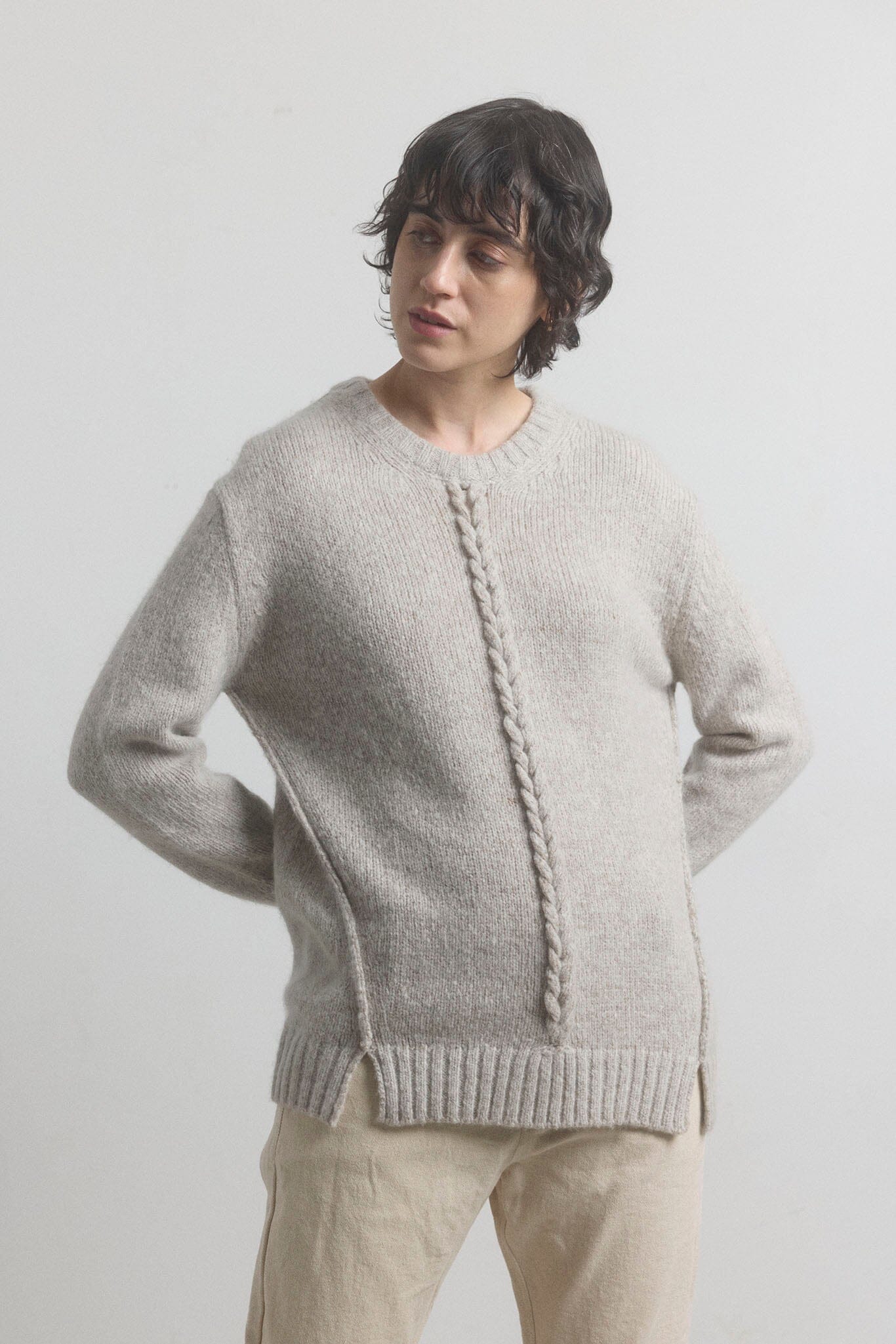 Woman wearing a light gray knitted sweater on a plain background
