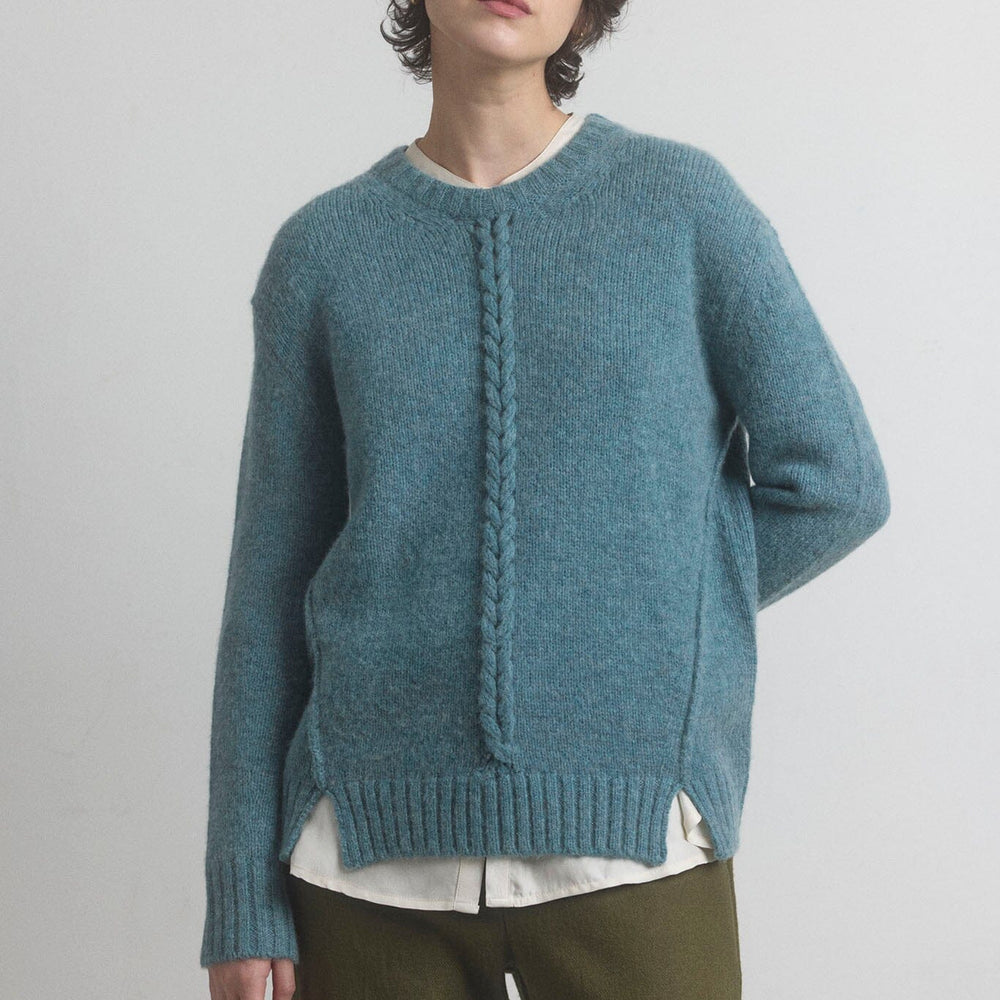 Woman wearing a teal blue merino knit sweater with a white shirt underneath on a plain background