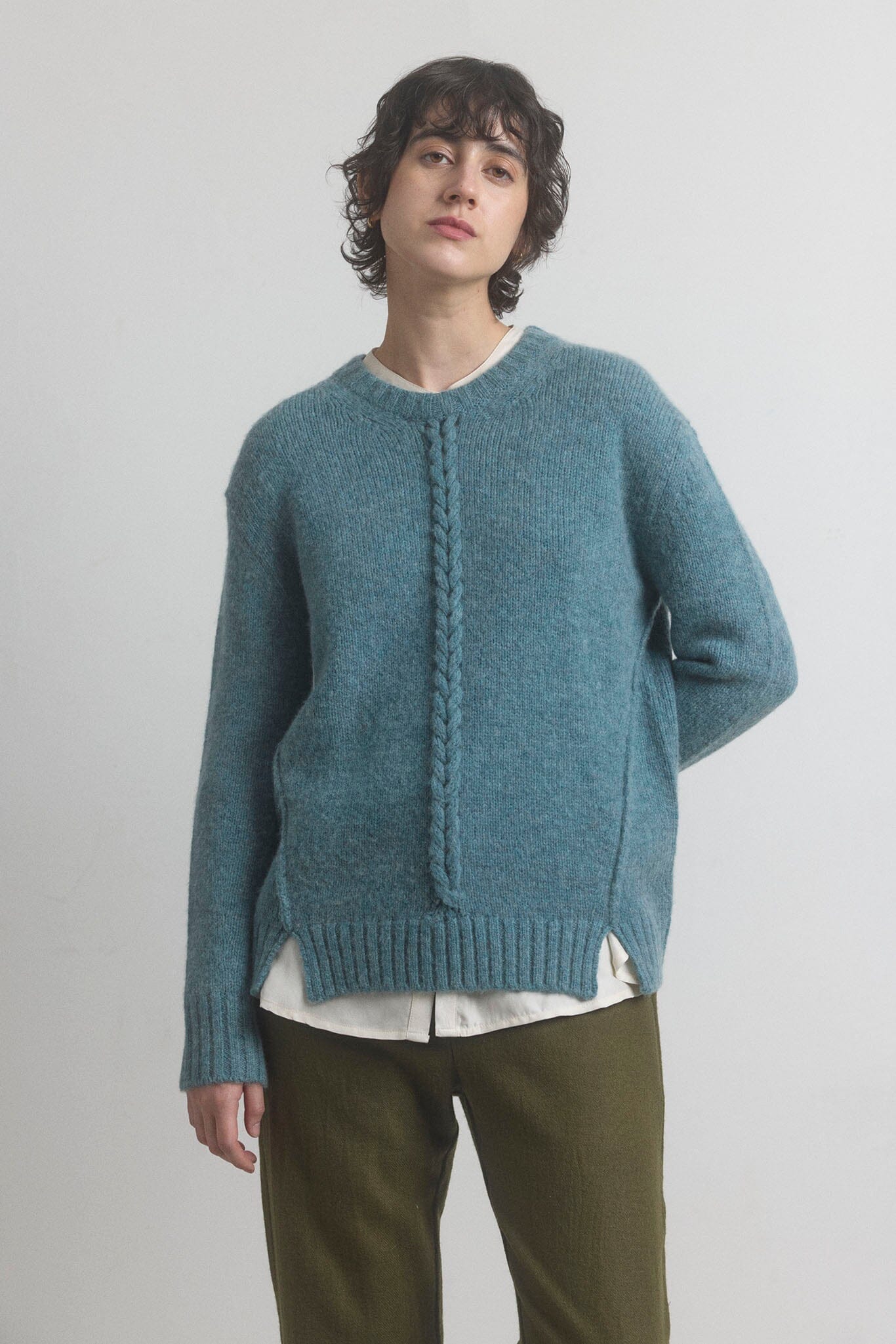 Woman wearing a teal blue merino knit sweater with a white shirt underneath on a plain background