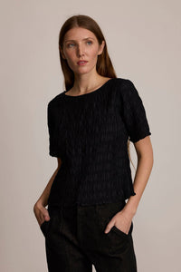 Woman wearing the M.PATMOS Miwa Smocked Top in Black, featuring a fitted bodice and boat neckline.