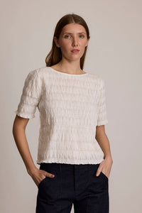 Woman wearing the M.PATMOS Miwa Smocked Top in Ivory Jacquard, featuring a fitted bodice and boat neckline.