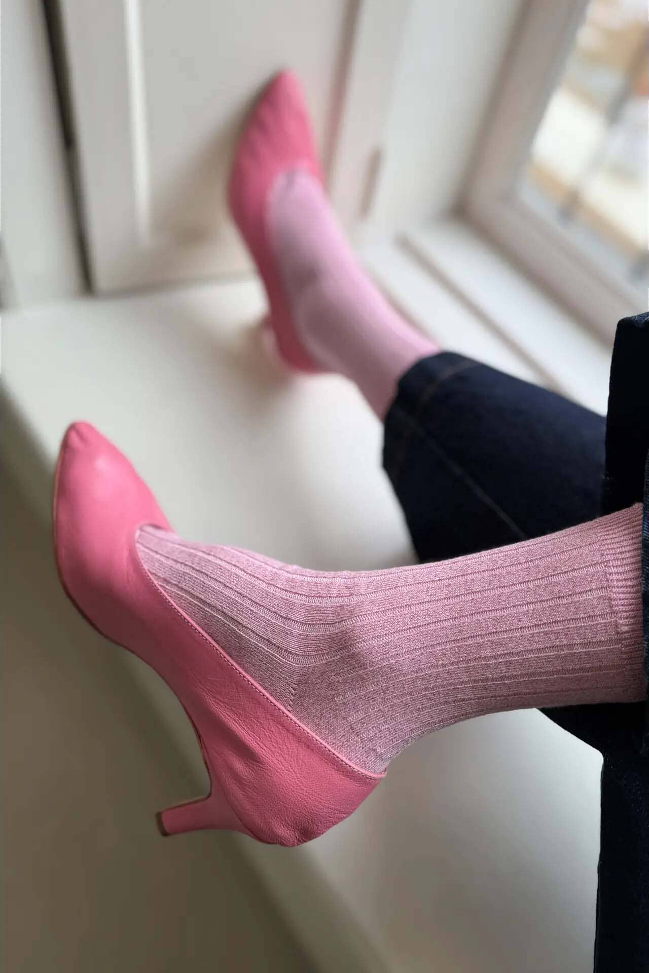 Pink high heels and pink ribeed socks on a white surface