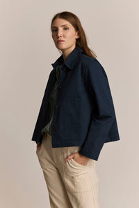 Woman wearing a navy blue chore jacket and beige pants against a plain background