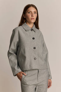 Woman wearing a cropped grey striped chore jacket against a beige background