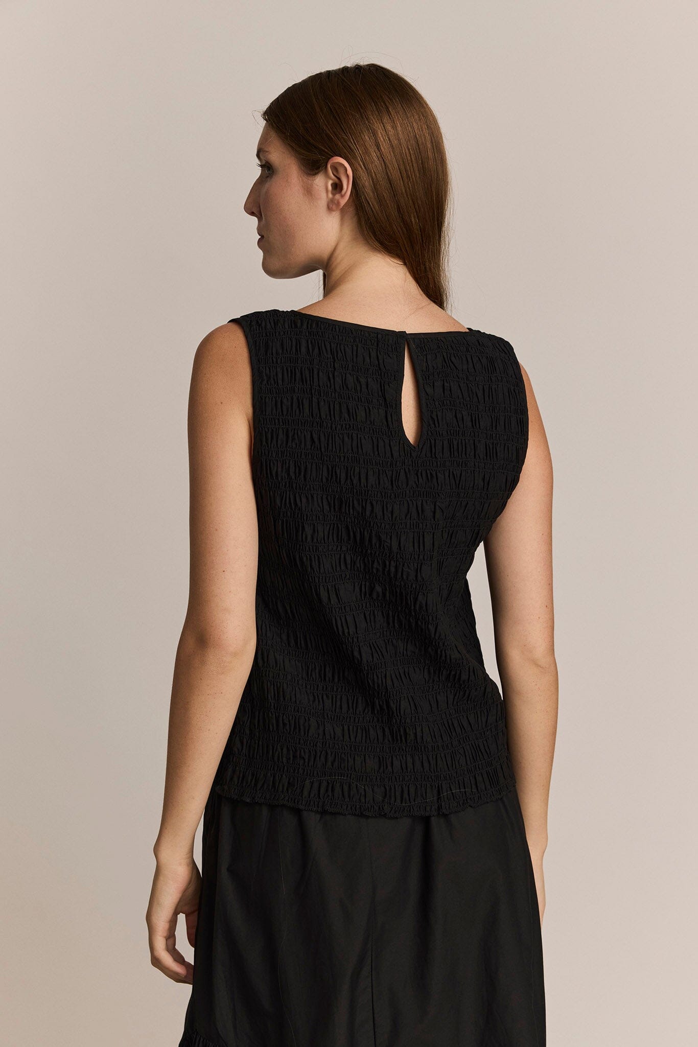 Woman wearing a black gathered sleeveless top against a beige background