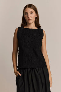 Woman wearing a black gathered sleeveless top against a neutral background