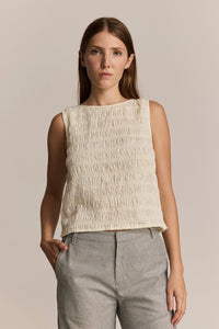Woman wearing a textured ivory sleeveless top and striped grey pants against a neutral background