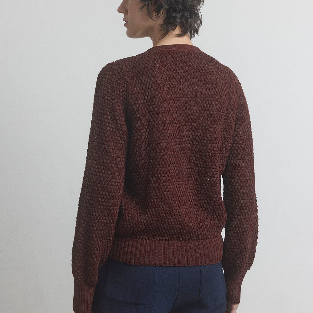 Person wearing a dark berry knitted sweater and dark blue pants on a light gray background.