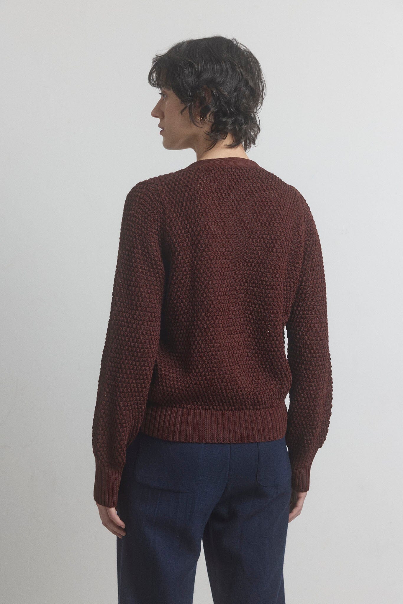 Person wearing a dark berry knitted sweater and dark blue pants on a light gray background.