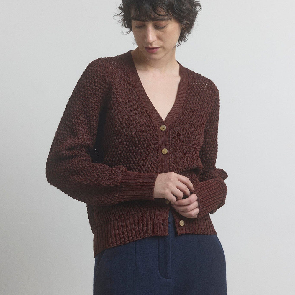 Person wearing a dark berry knitted button down cardigan with a plain background.