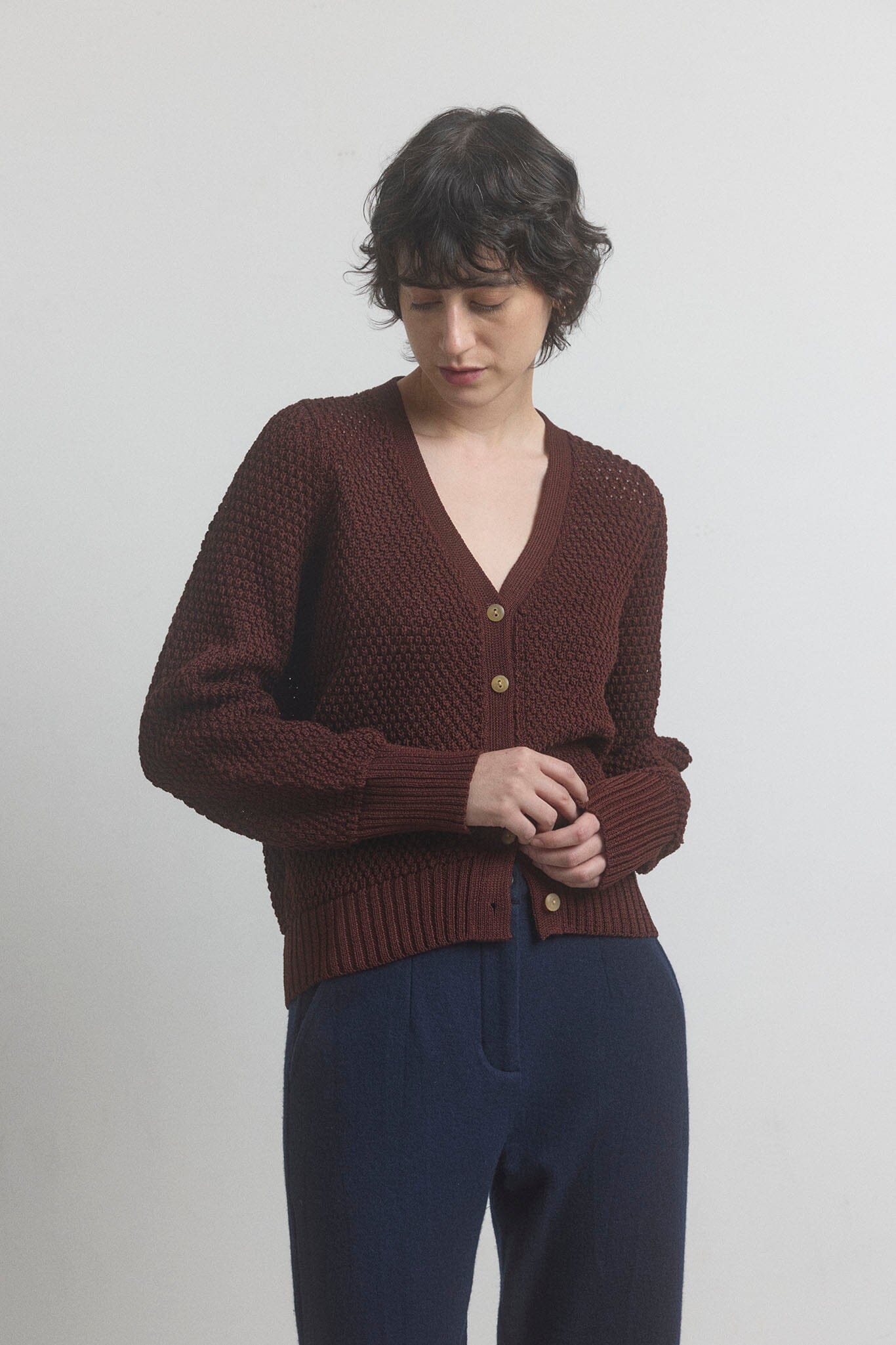 Person wearing a dark berry knitted button down cardigan with a plain background.