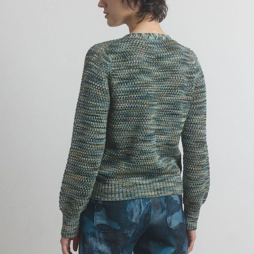 Person wearing a green textured sweater and blue pants on a plain background