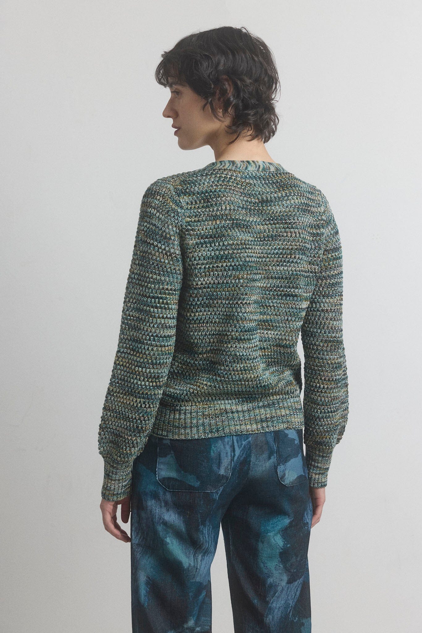 Person wearing a green textured sweater and blue pants on a plain background