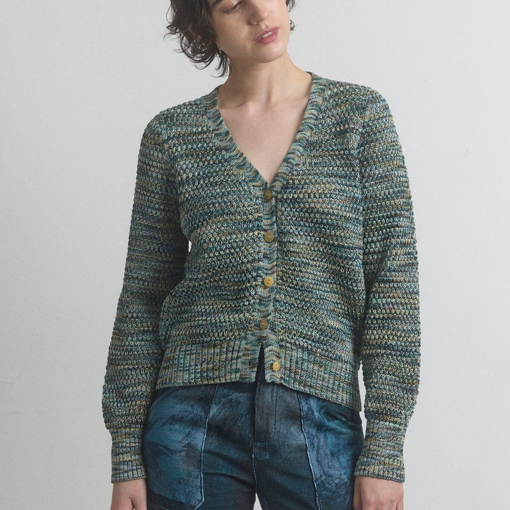 Woman wearing a green knitted cardigan and blue jeans against a plain background