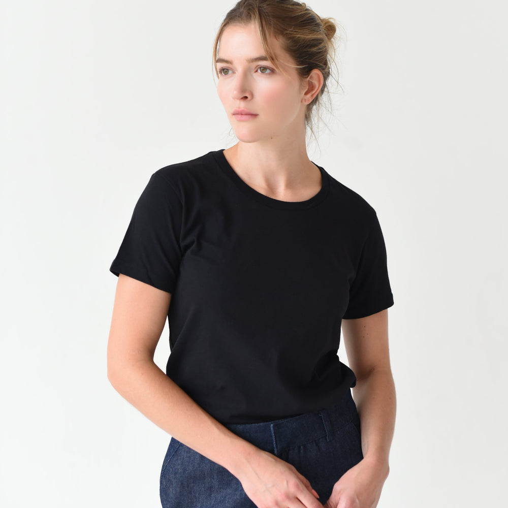 
                  
                    A woman wearing a black Mott Tee and blue jeans, standing against a white background.
                  
                