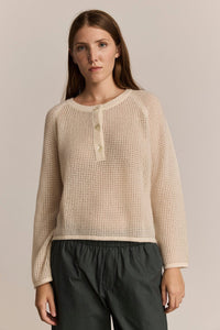 Woman wearing an ivory textured henley sweater with black pants against a plain background