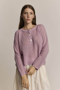 Woman wearing a pink cashmere knit long sleeve sweater against a plain background
