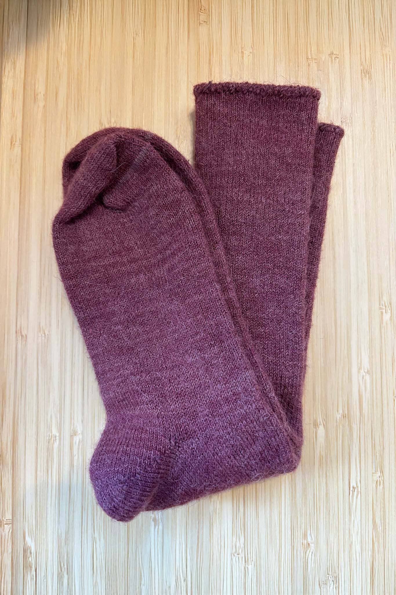 Pair of berry colored socks on a wooden surface.