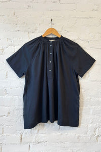 Black short sleeve summer blouse on a hanger against a white brick wall