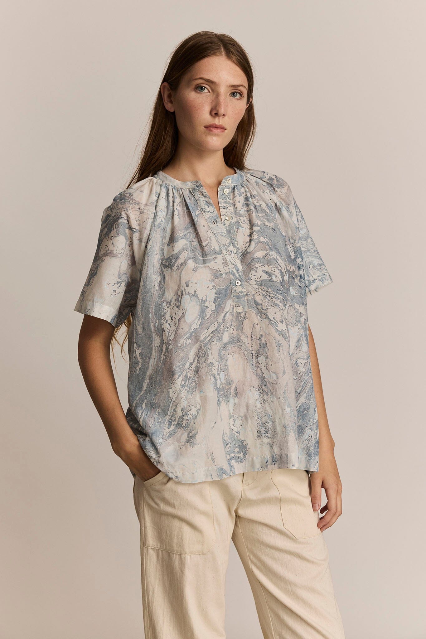 Woman wearing a short sleeve floral blouse and beige pants against a neutral background