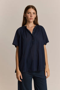 Woman wearing a short sleeve, lightweight, navy blue blouse against a beige background