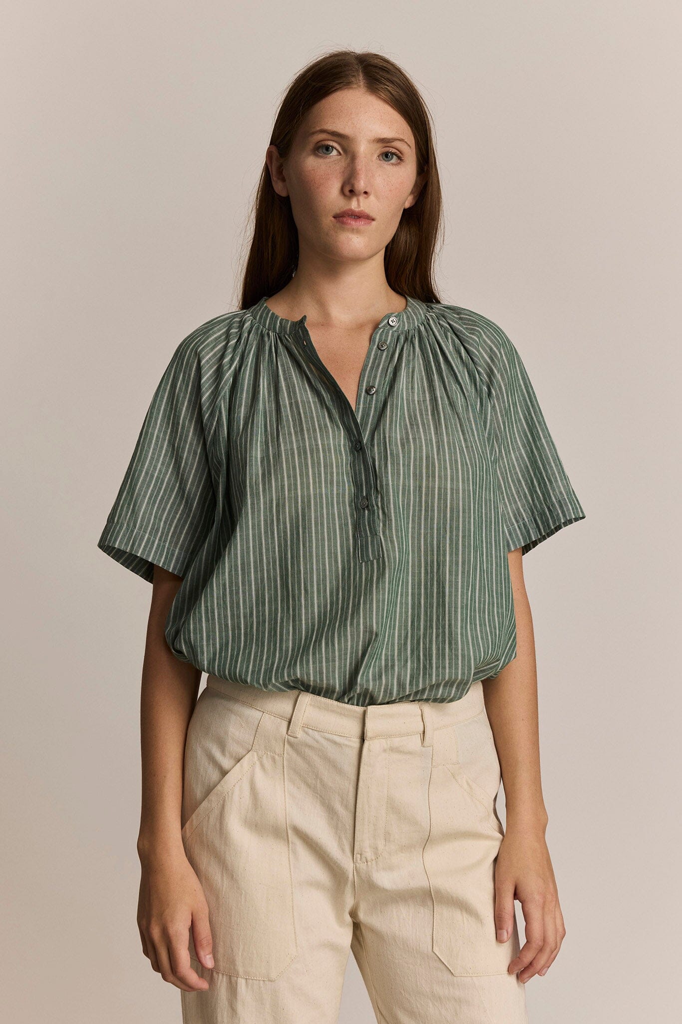 Woman wearing a short sleeve green striped shirt and beige pants against a beige background