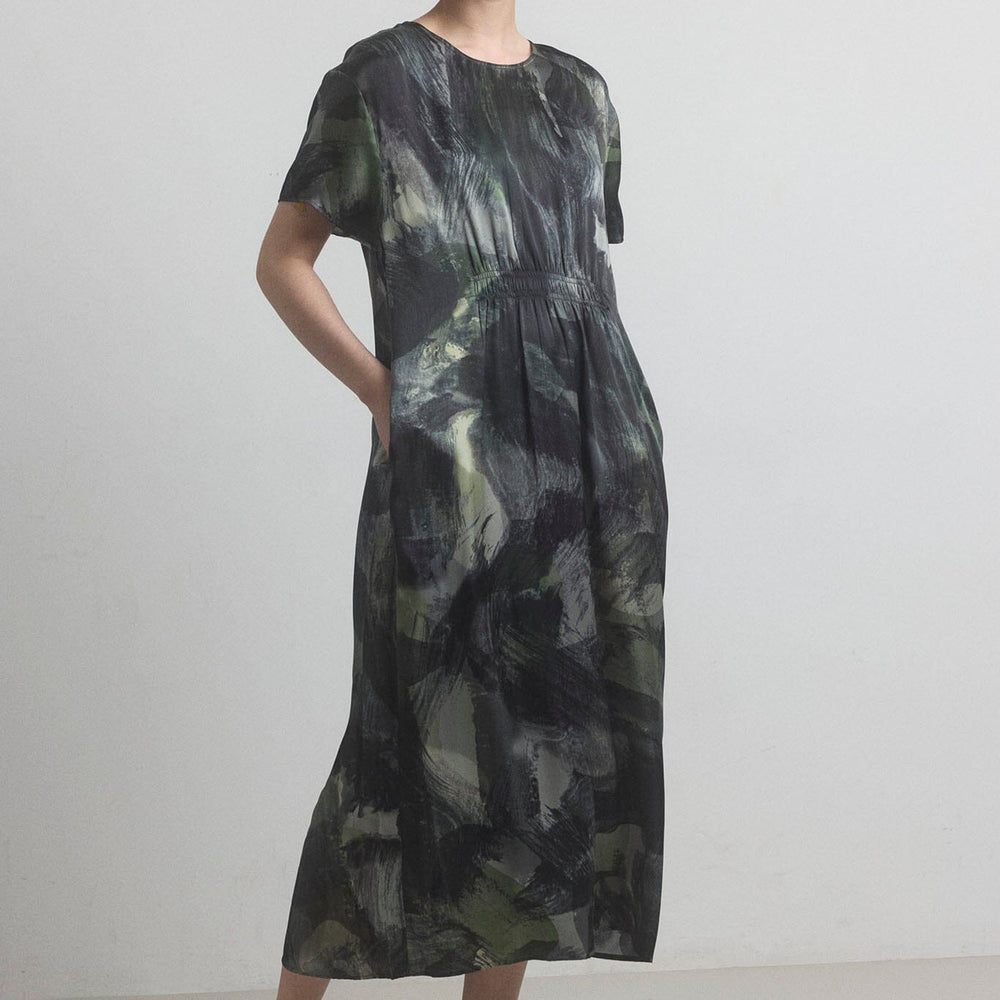 Woman wearing a black and green patterned silk dress from M.PATMOS on a plain background