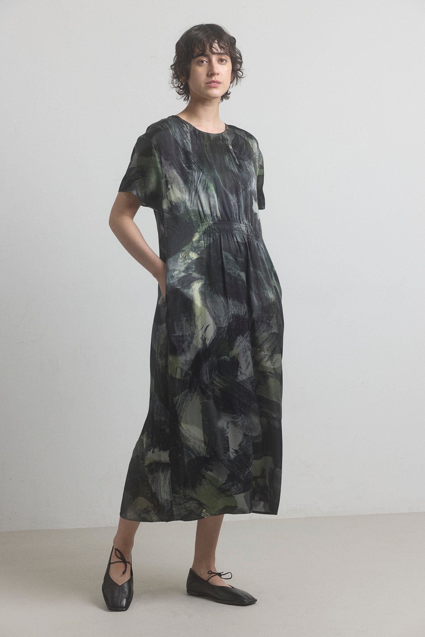 Woman wearing a black and green patterned silk dress from M.PATMOS on a plain background