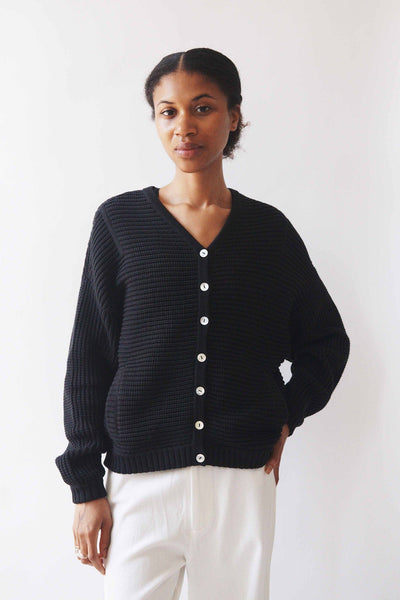 A woman wears the M.Patmos cotton Putnam long sleeve sweater in black. The fabric has a textured stitch and features natural horn buttons down the front.