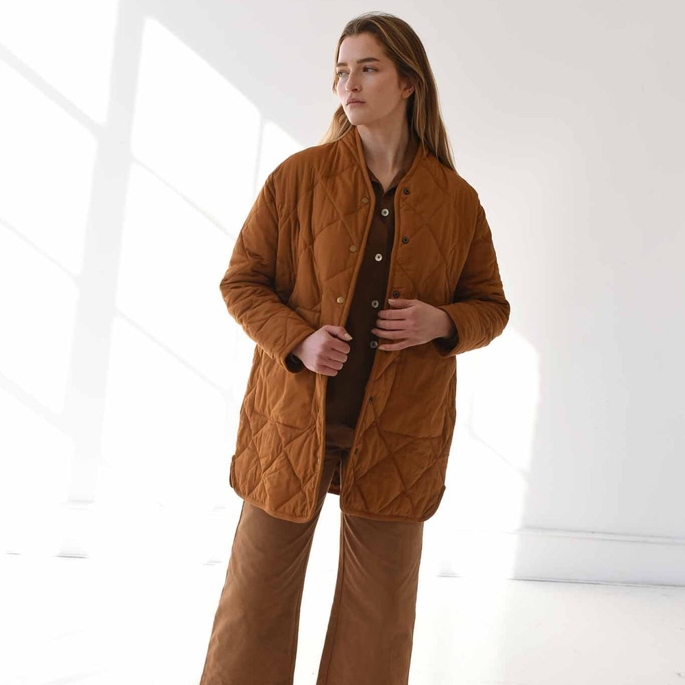 A woman wears the M.Patmos quilted Sana coat in rich caramel color. Snap buttons down the front with two pockets.