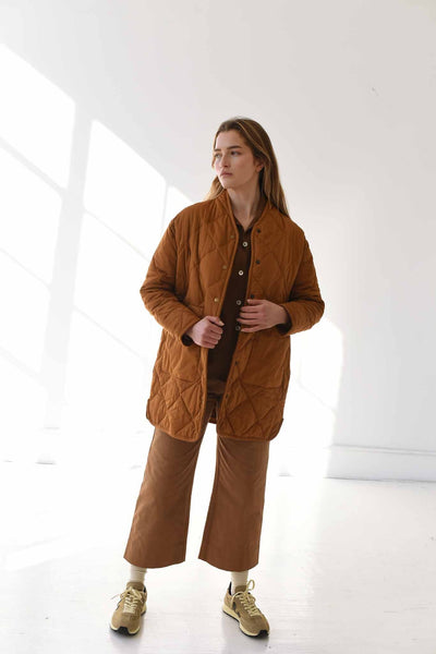 A woman wears the M.Patmos quilted Sana coat in rich caramel color. Snap buttons down the front with two pockets.