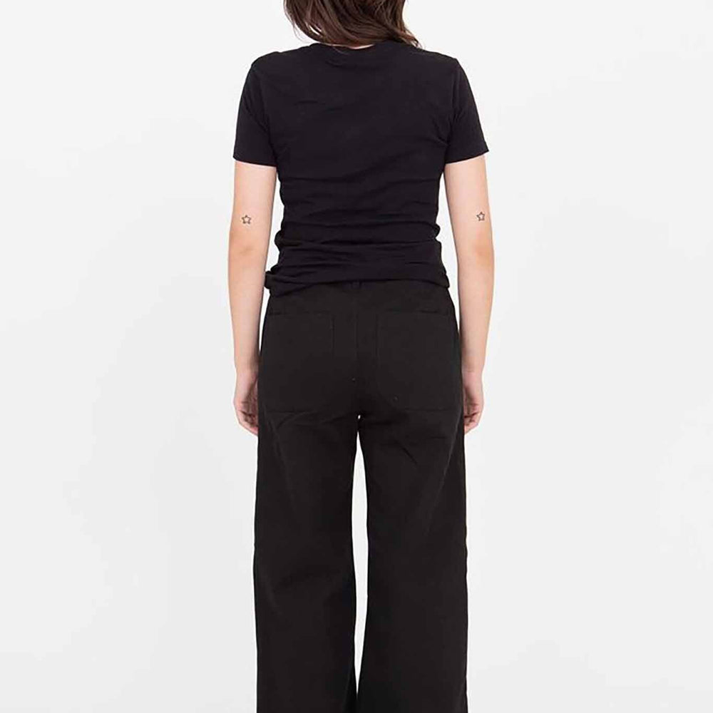 A woman standing, wearing black Riverside pants with a wide leg and a black top. She has short hair and is posing with her hands on her hips.