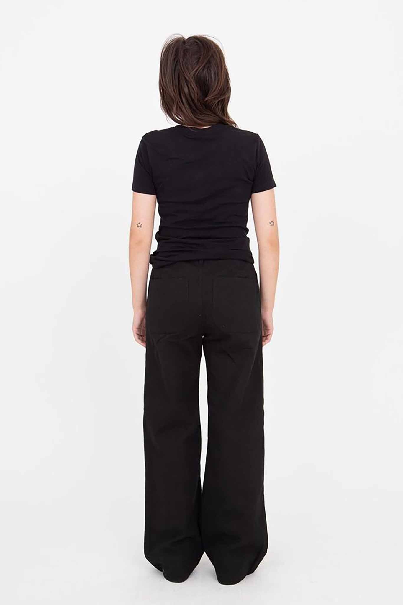 A woman standing, wearing black Riverside pants with a wide leg and a black top. She has short hair and is posing with her hands on her hips.