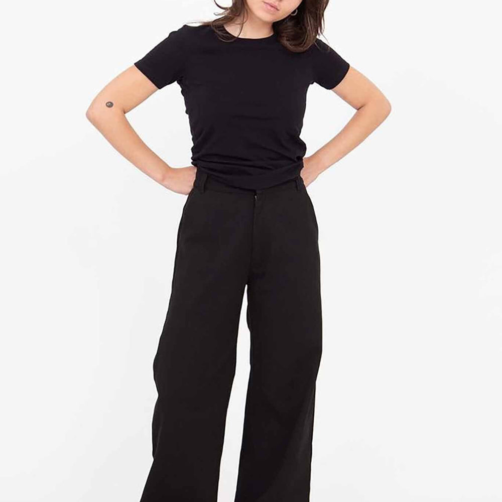A woman standing, wearing black Riverside pants with a wide leg and a black top. She has short hair and is posing with her hands on her hips.