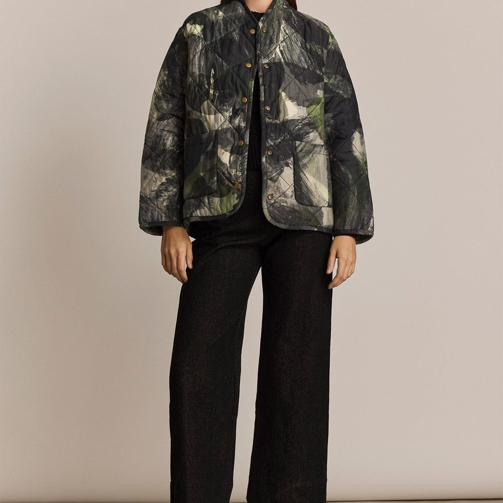 Woman wearing a patterned jacket and black pants on a beige background