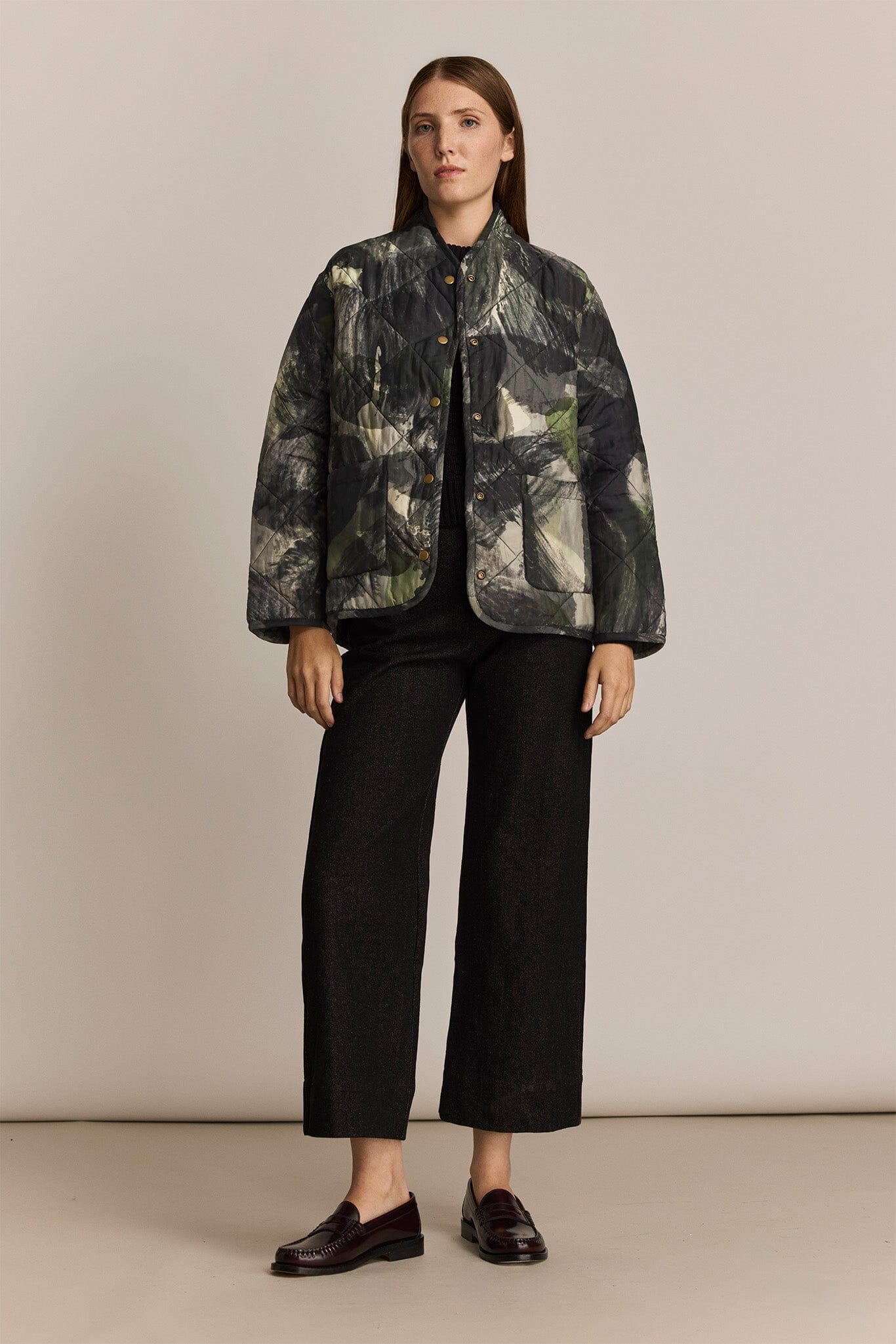 Woman wearing a patterned jacket and black pants on a beige background