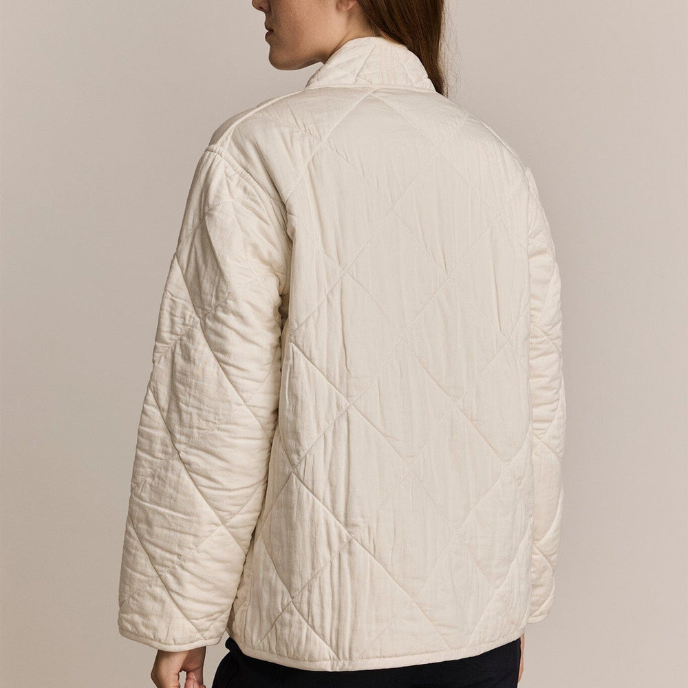Person wearing an ivory quilted jacket against a plain background