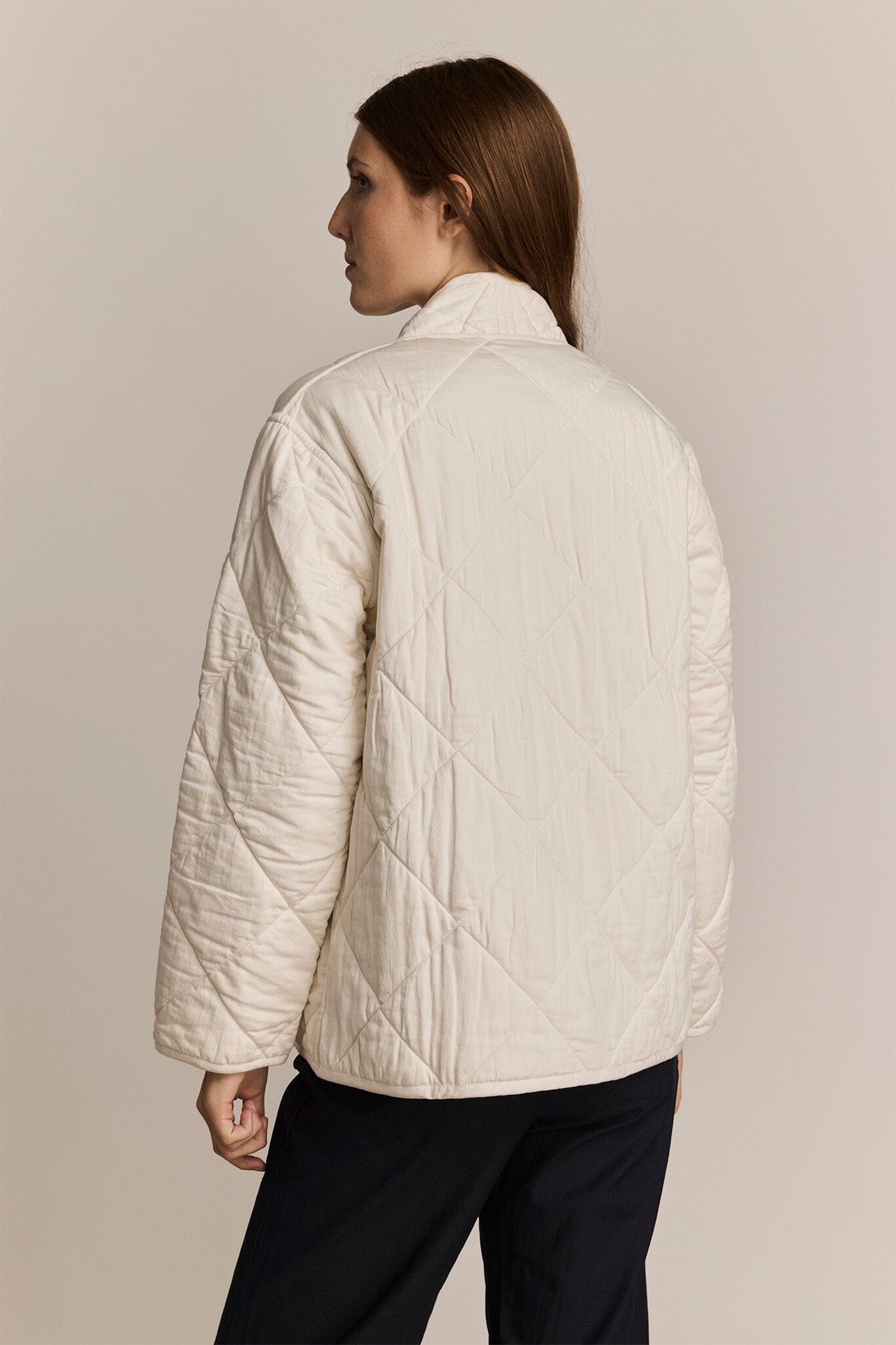 Person wearing an ivory quilted jacket against a plain background