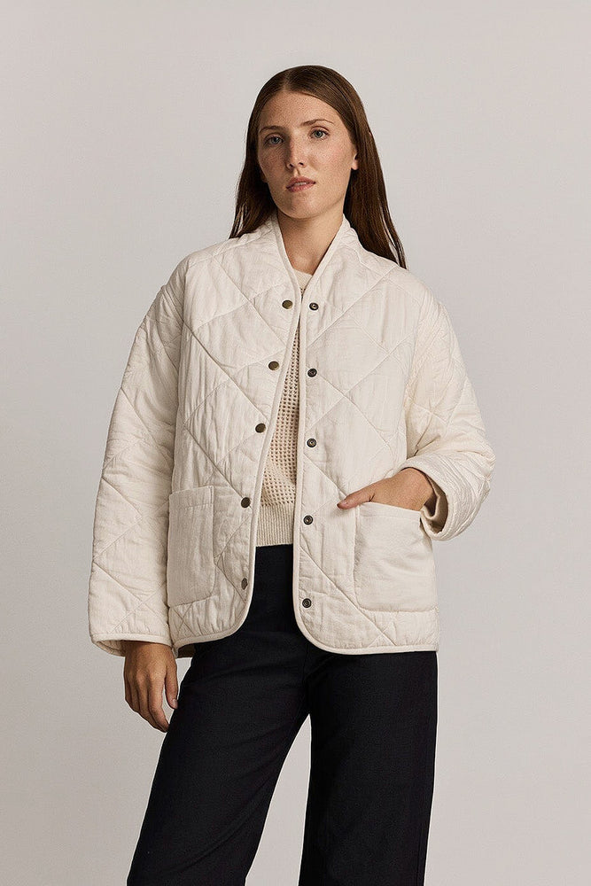 Woman wearing a white quilted jacket against a plain background