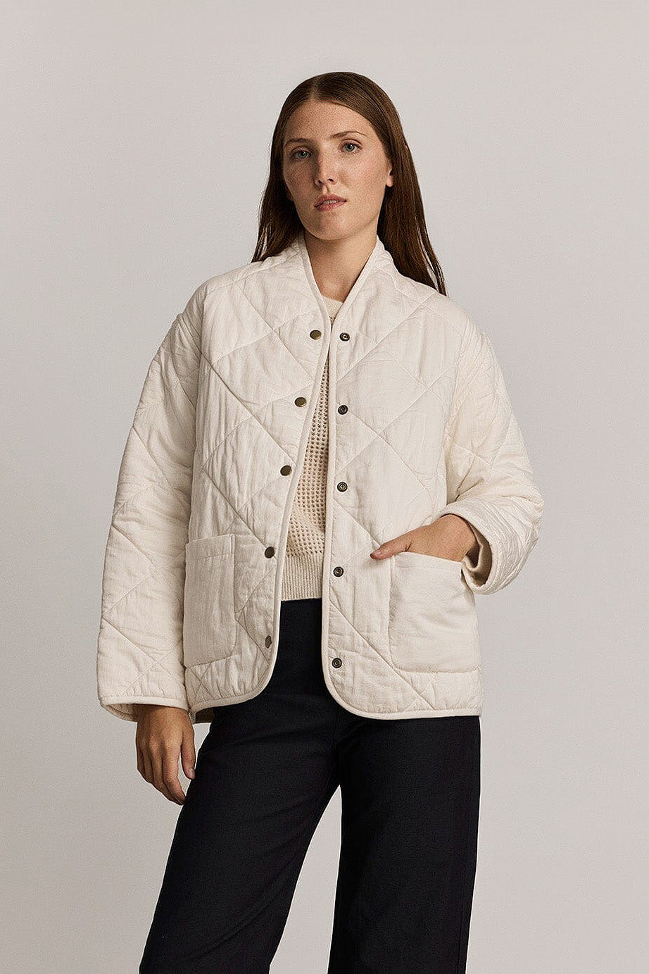 Woman wearing a white quilted jacket against a plain background