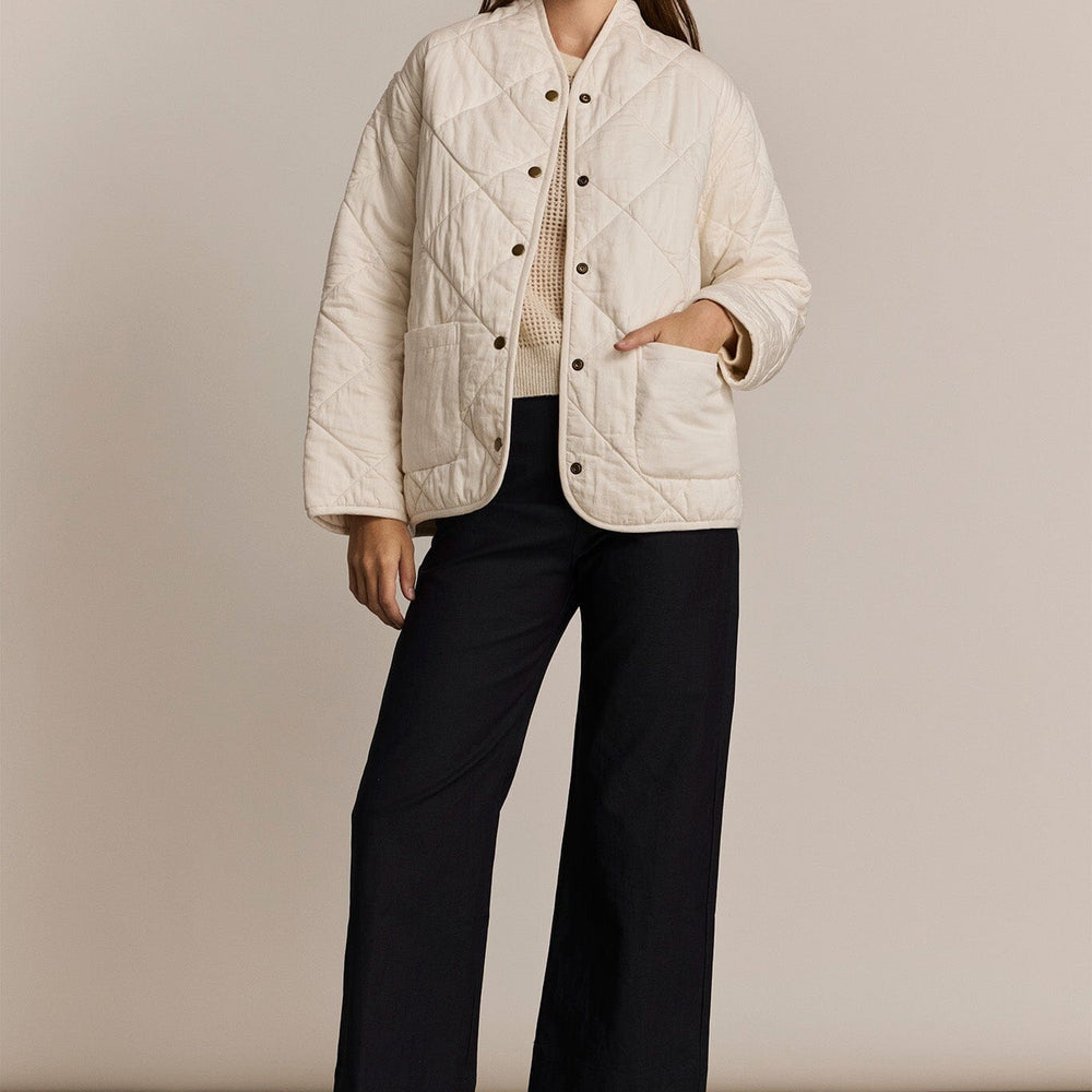 Woman wearing a white quilted jacket with black pants on a beige background
