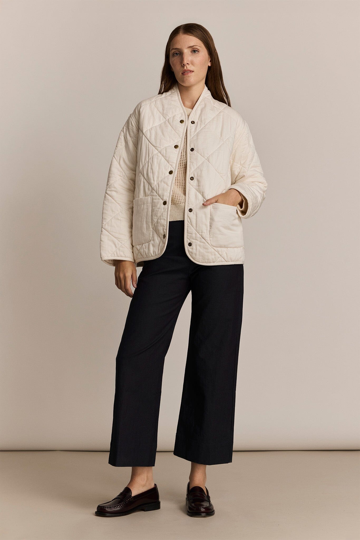 Woman wearing a white quilted jacket with black pants on a beige background