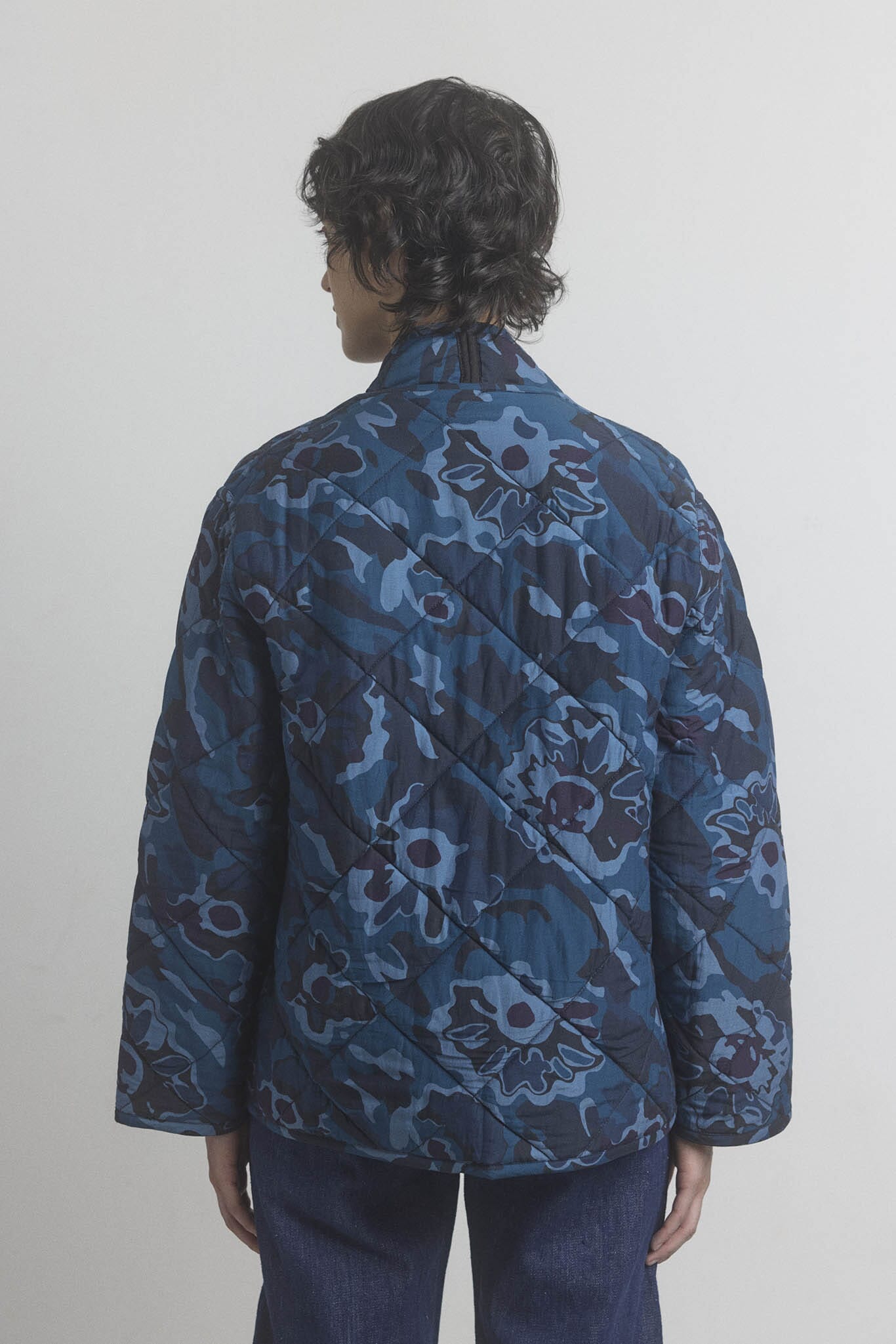 Person facing the back wearing a blue floral patterned jacket against a white background