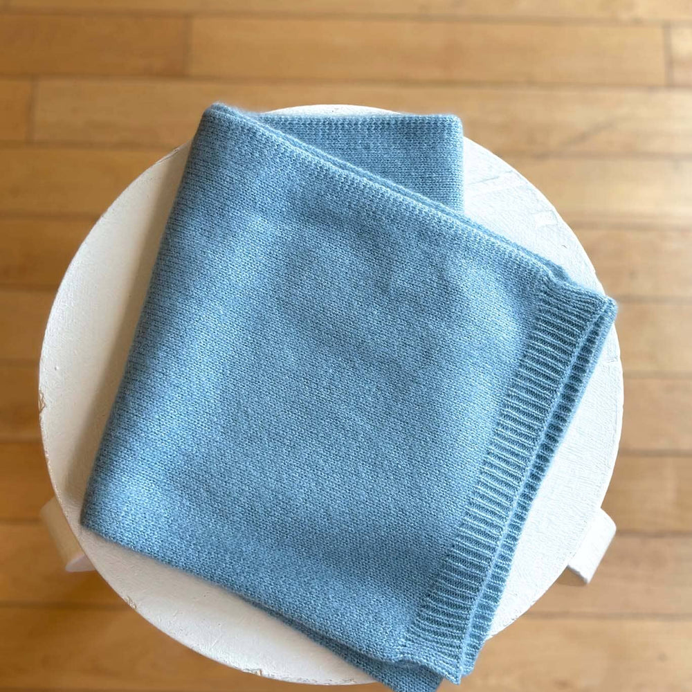 
                  
                    Blue soft knitted scarf on a white plate with a wooden floor background
                  
                
