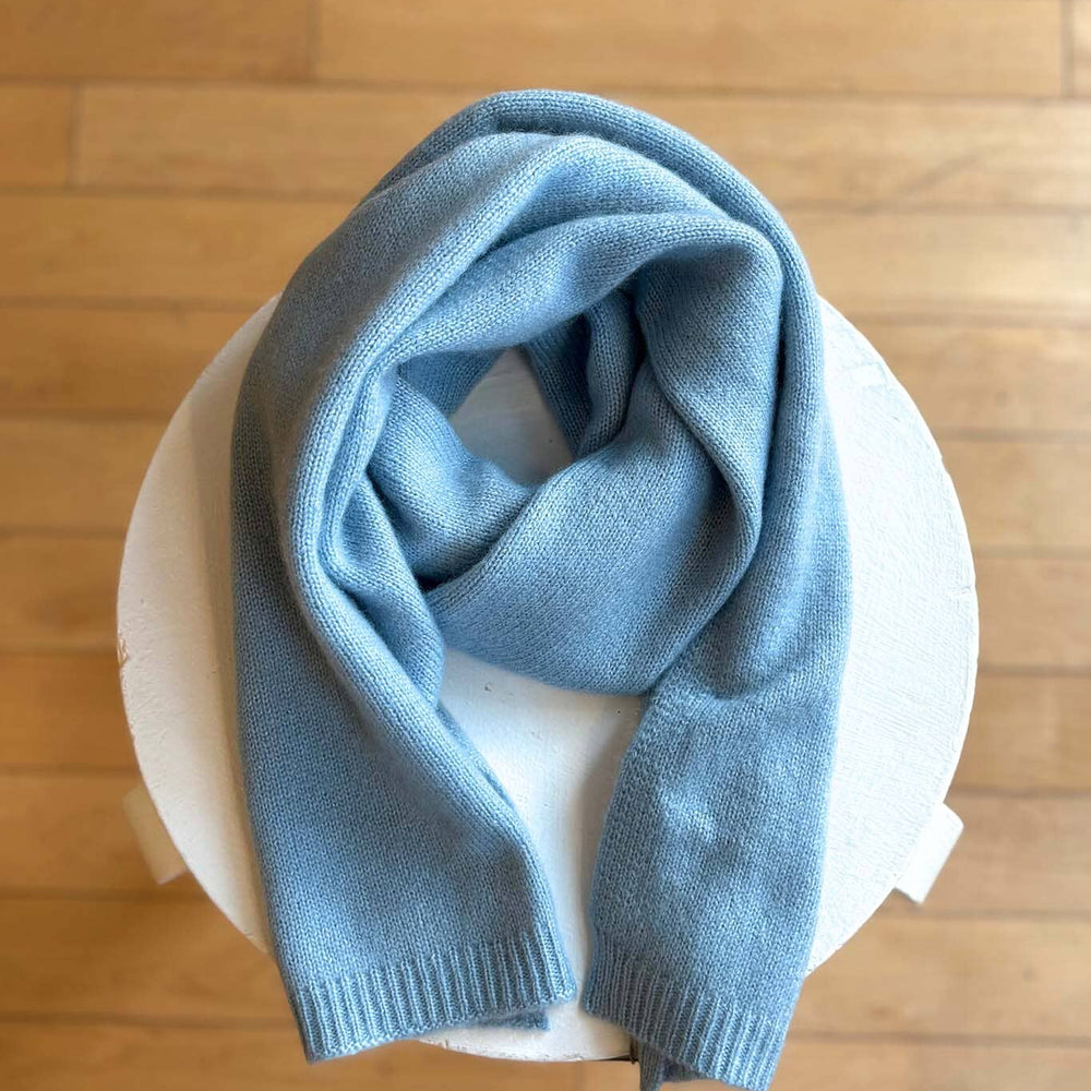 
                  
                    Light blue knit scarf on a white bowl with a wooden floor background
                  
                
