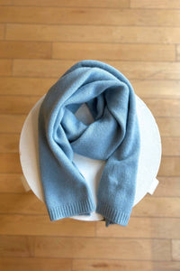 Light blue knit scarf on a white bowl with a wooden floor background