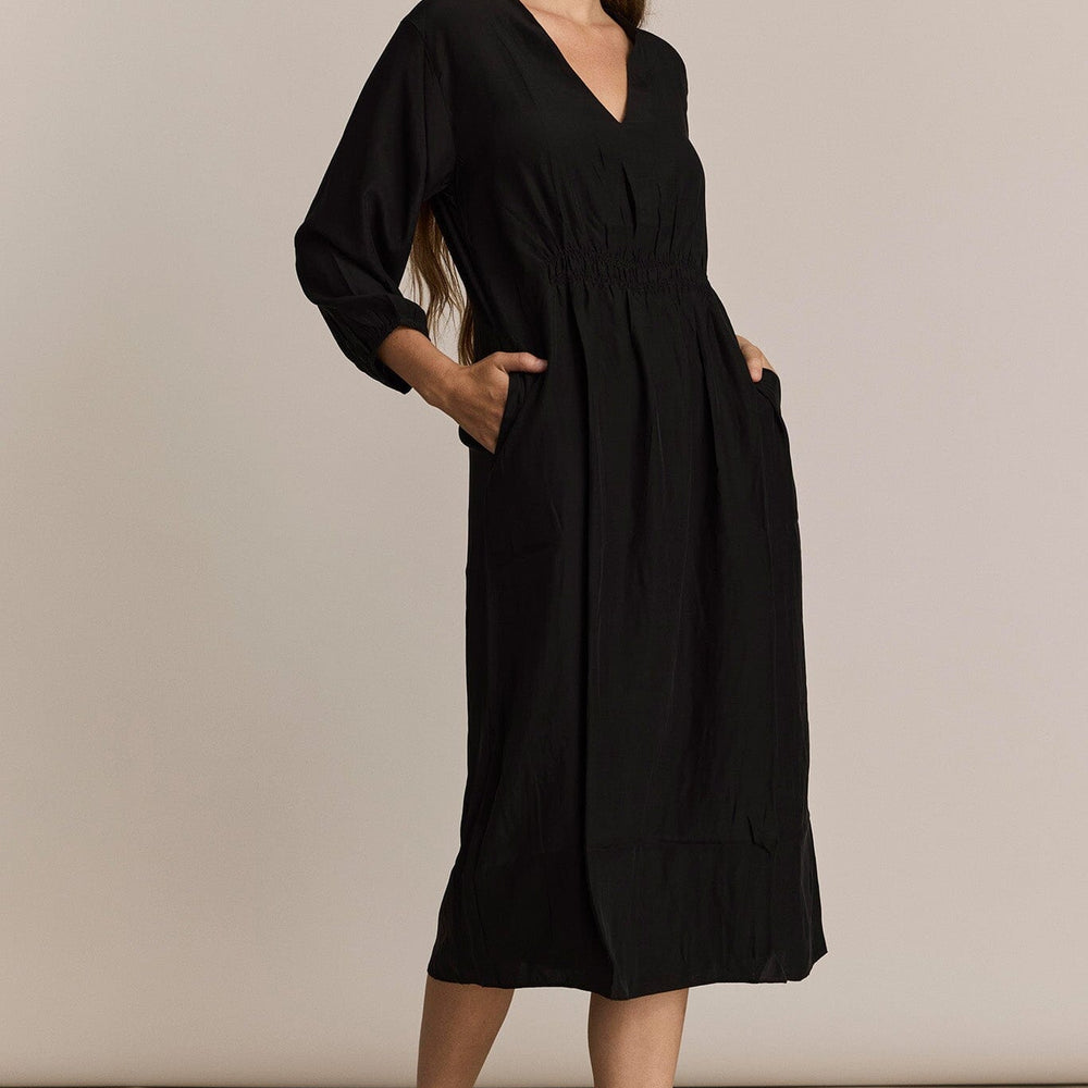 Woman wearing a black dress with long sleeves against a beige background