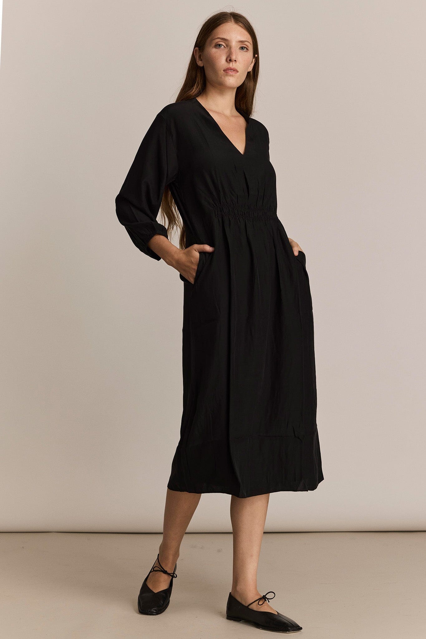 Woman wearing a black dress with long sleeves against a beige background