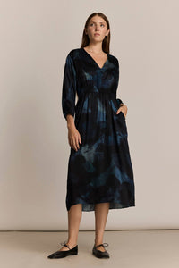 Woman wearing a midi-length blue patterned three quarter inch sleeve dress against a plain background